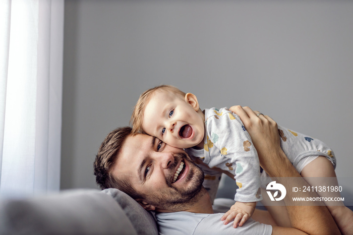 Young attractive caring father holding his beloved little son, singing song to him and having fun.