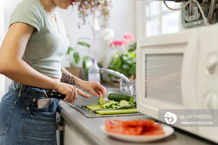 Midsection of young woman chopping vegetables in kitchen