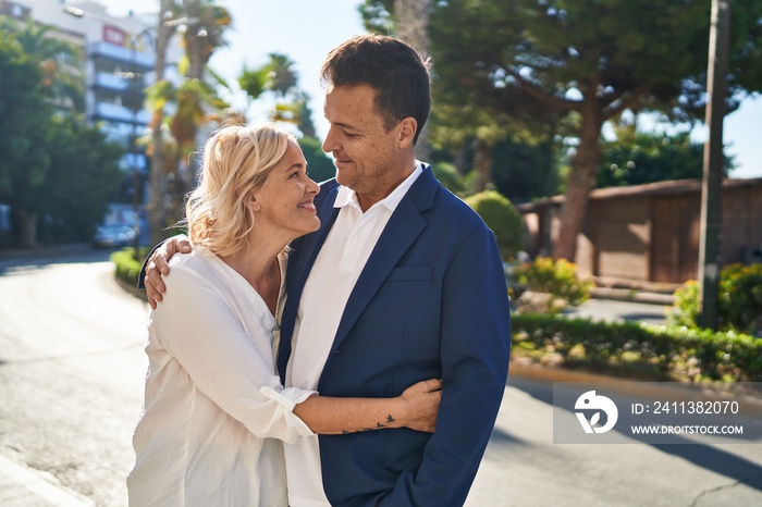 Middle age man and woman couple hugging each other standing at street