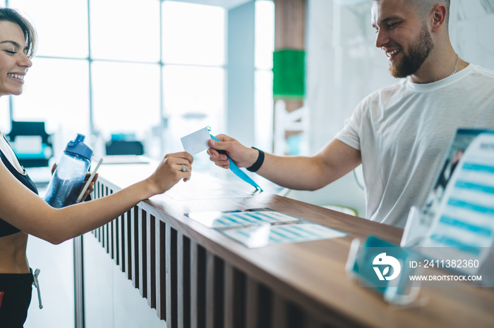 Cropped image of caucasian female standing with male employee for gym talking to each other and taking card for access, happy slim woman 20s client communicating with man receptionist