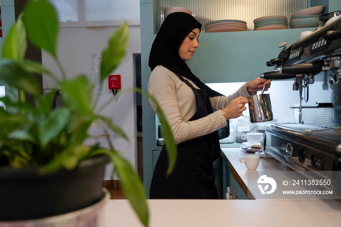 Young woman in hijab making coffee in cafe