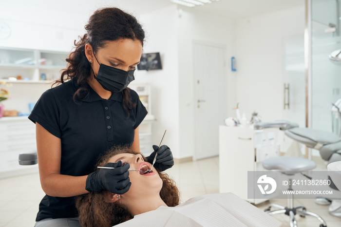 Female dentist in uniform examining oral cavity of patient