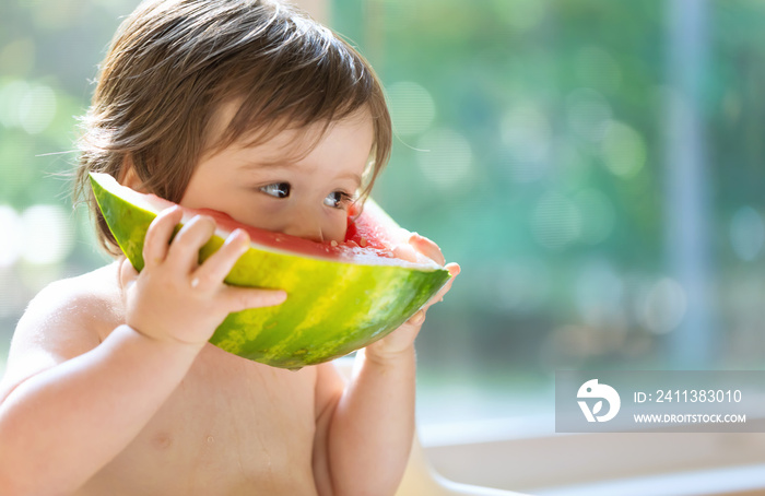 Toddler boy eating watermelon in his highchair