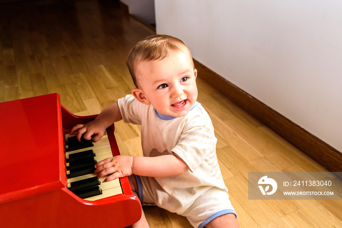 Smiling baby playing a toy piano while learning music.