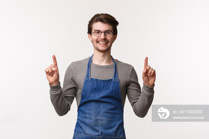 Happy, friendly-looking bartender invite visit his place, pointing fingers up and smiling camera joyfully as wearing apron at work, make coffee for customer, show upstairs seats, white background