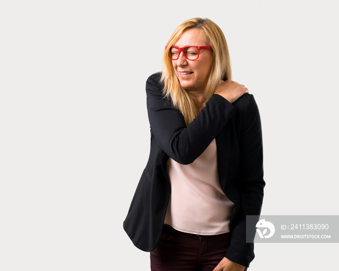 Middle-age blonde business woman with black jacket suffering from pain in shoulder for having made an effort on isolated grey background