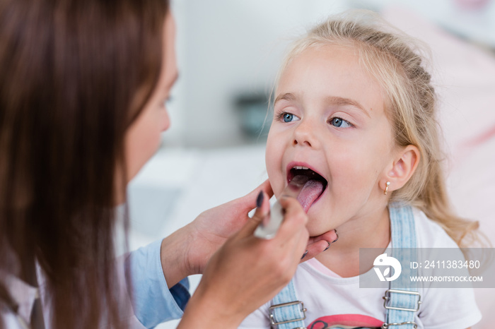 Little girl opening mouth in front of clinician examining her throat