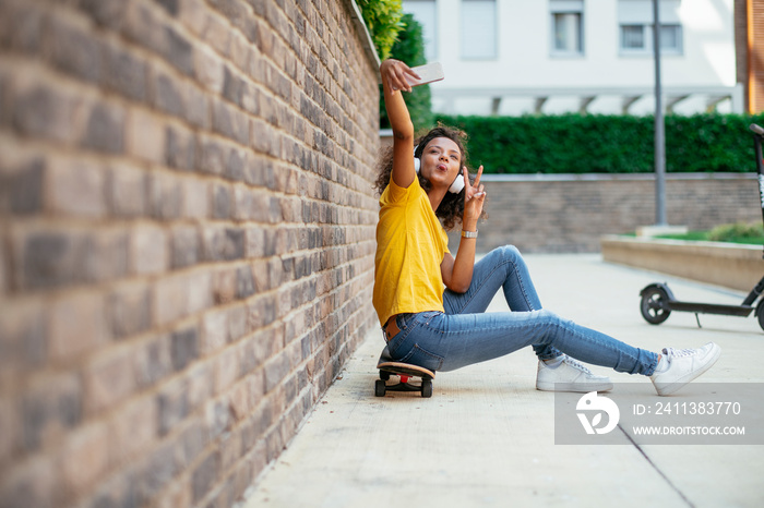 Beautiful afro girl taking selfie while sitting on skateboard