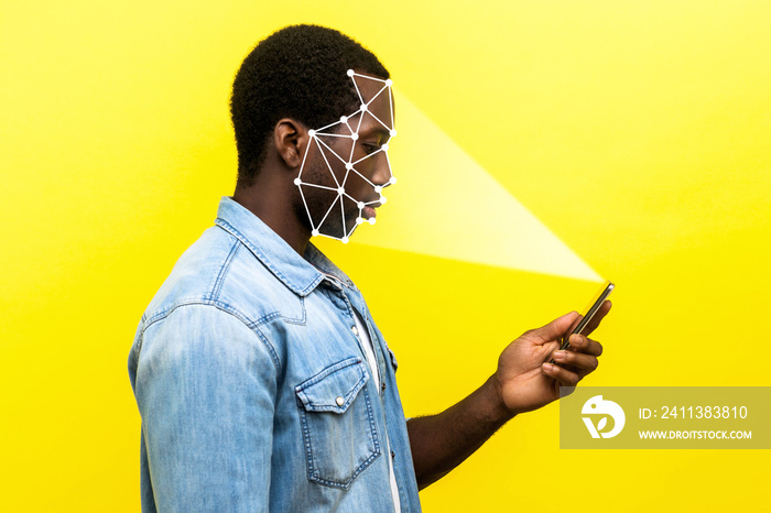 Mobile biometric identification and verification or detection concept. face ID scaning or unlocking technology. serious man using facial recognition on smartphone. indoor isolated on yellow background