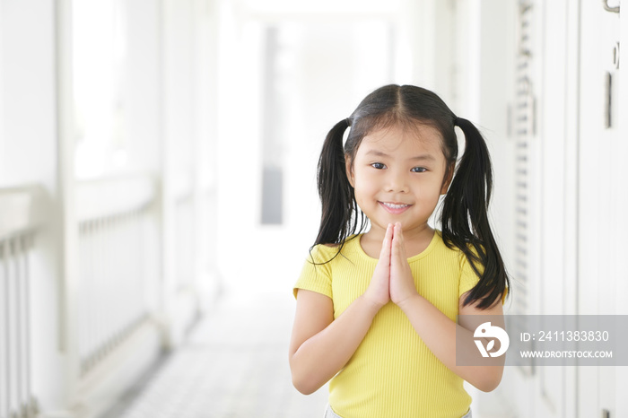 Asian child smiling hand in hand or kid girl pay obeisance and pray or hello welcome and thank you with wear yellow shirt in morning at church or temple for peace on white house receptionist at hotel