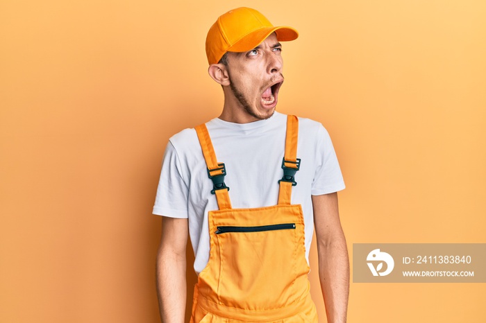 Hispanic young man wearing handyman uniform angry and mad screaming frustrated and furious, shouting with anger. rage and aggressive concept.