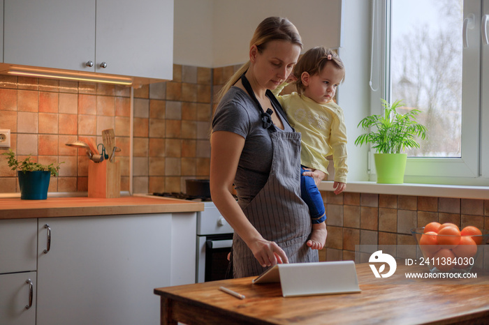 Mother with her baby girl looking for recipe on digital tablet