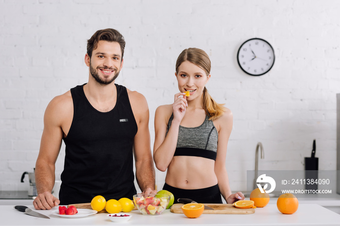 happy man smiling near woman eating sliced orange in kitchen