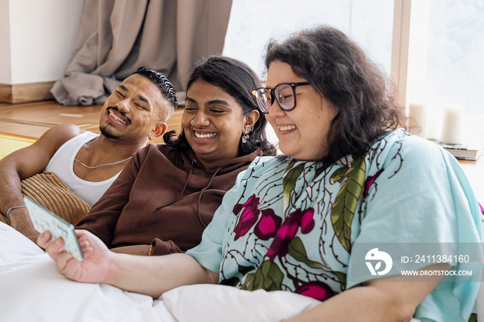 Three friends chatting and laughing together at home in bed