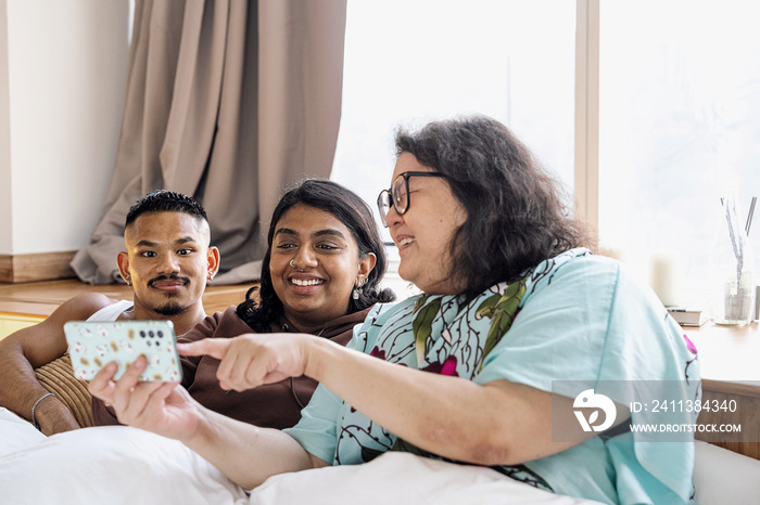 Three friends chatting and laughing together at home in bed