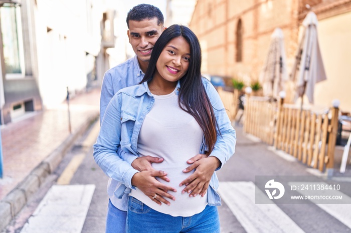 Young latin couple expecting baby hugging each other standing at street