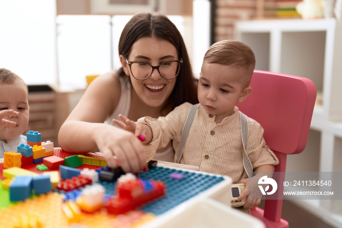 Teacher and preschool student playing with construction blocks sitting on table at kindergarten