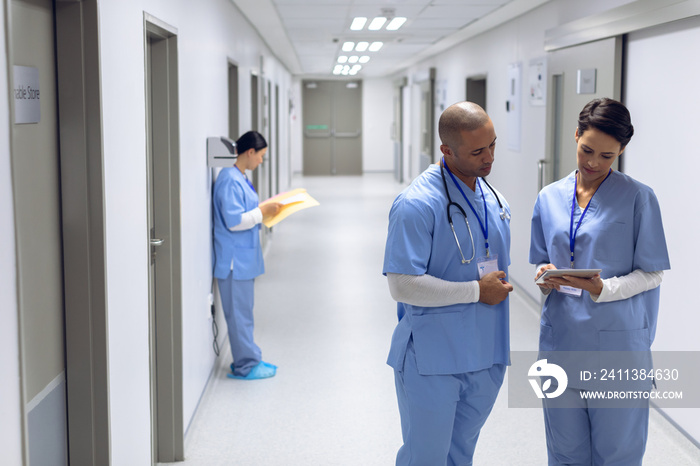 Two surgeons discussing over digital tablet in corridor at hospital