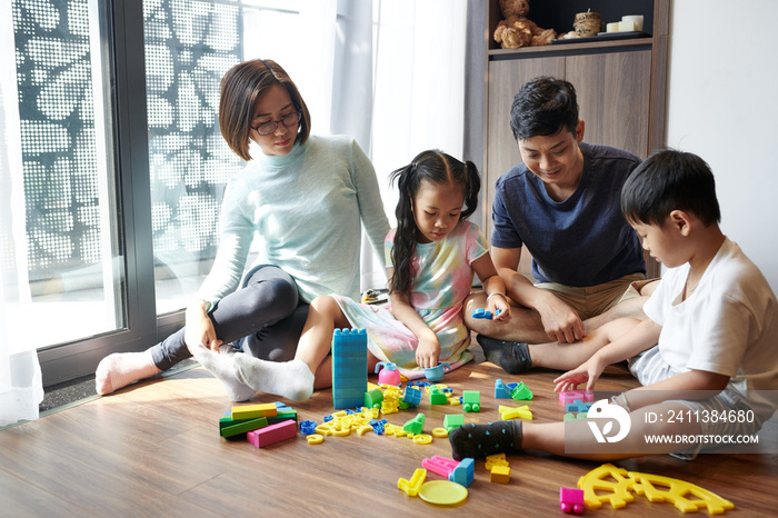 Asian parents and children playing together at home with plastic figures and colorful building blocks