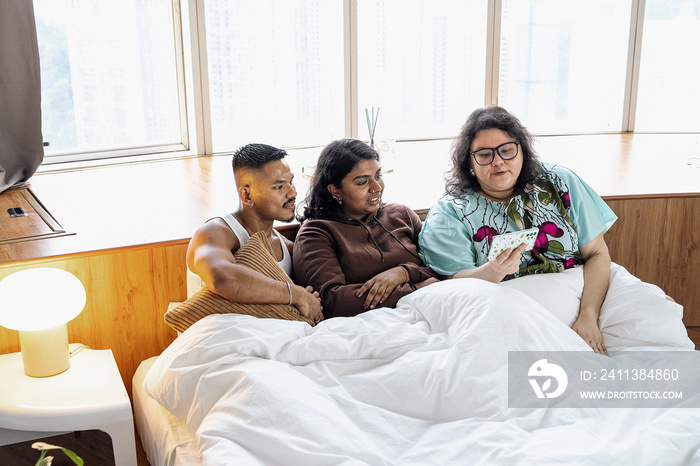 Three friends chatting and laughing together at home in bed