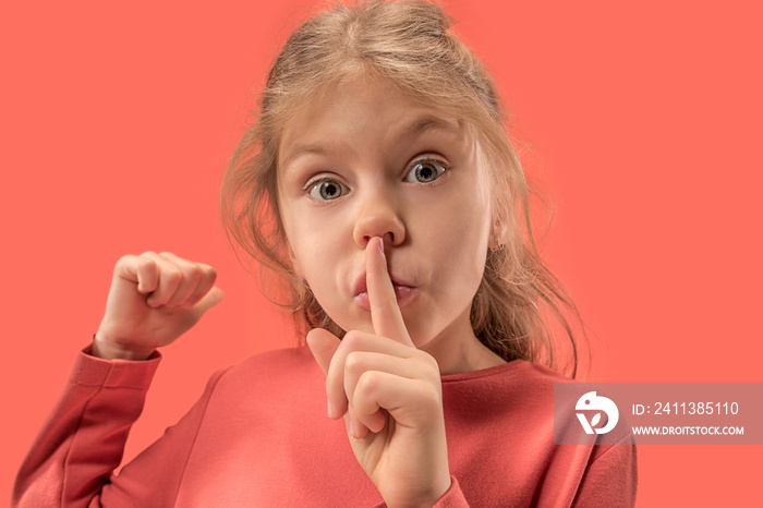 Young girl with her finger on her mouth on coral background. Human emotions and facial expression over trendy color