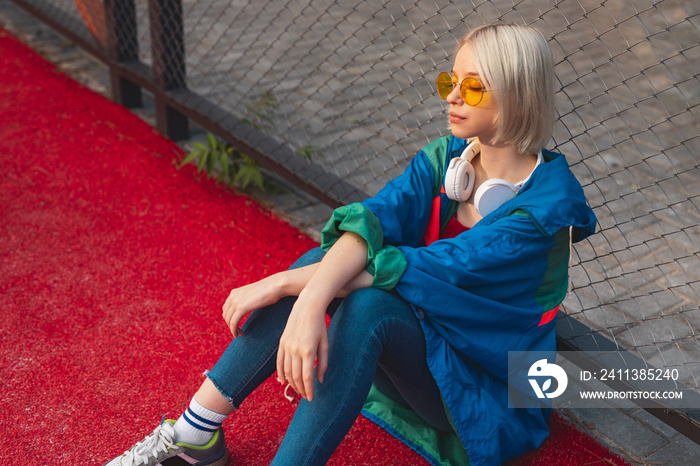 Trendy teenager resting on sports ground near fence