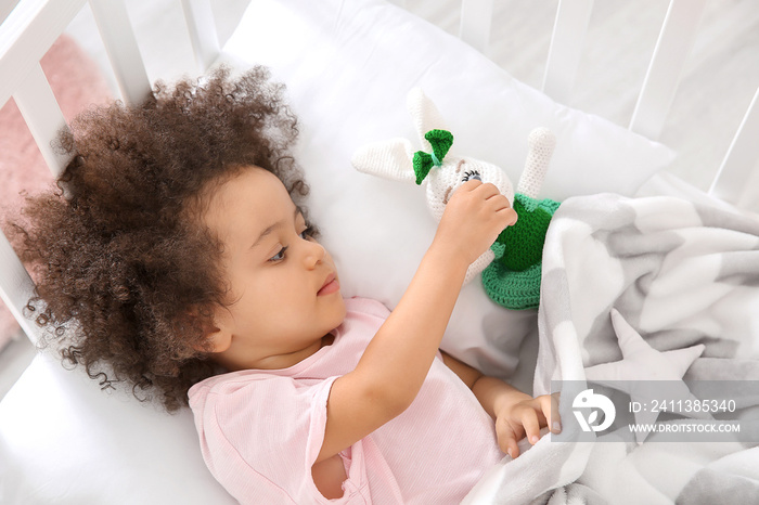 Little African-American girl with toy lying in bed