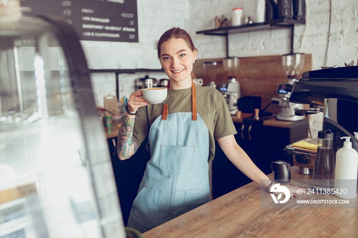 Joyful female barista with cup of coffee working in cafe