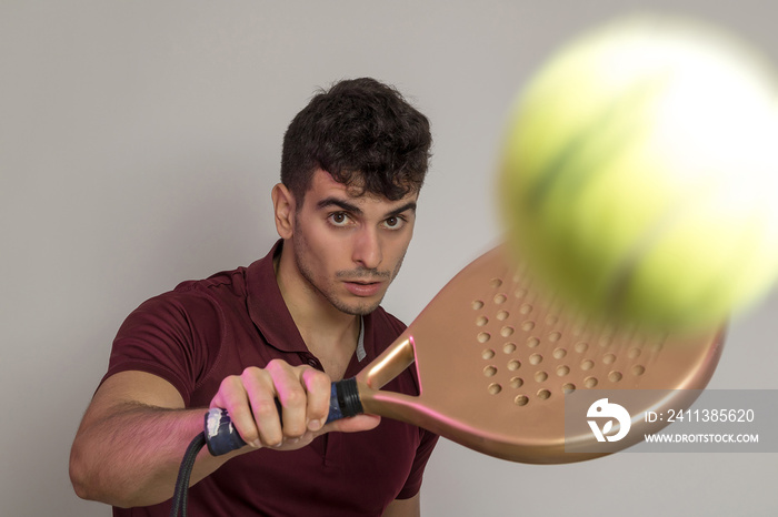 a young man posing with a paddle racket in a studio background.