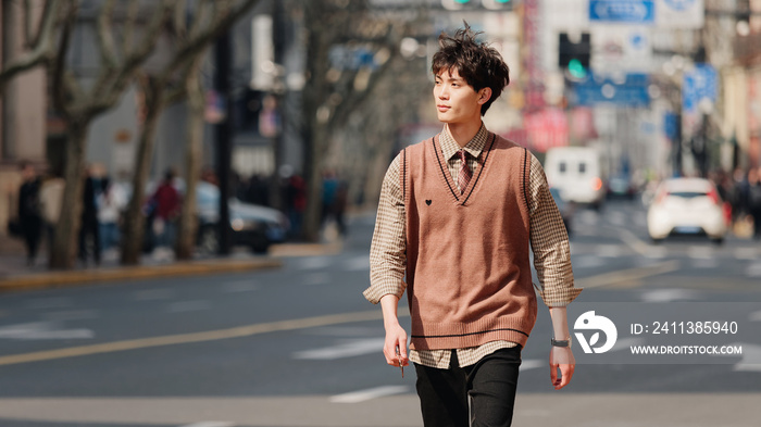 Portrait of a handsome Chinese young man with Korean style clothes walking on street in hurry in sunny day with Shanghai Nanjing road background, male fashion, cool Asian young man lifestyle.