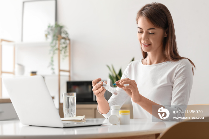 Beautiful woman with container of vitamin supplements in kitchen