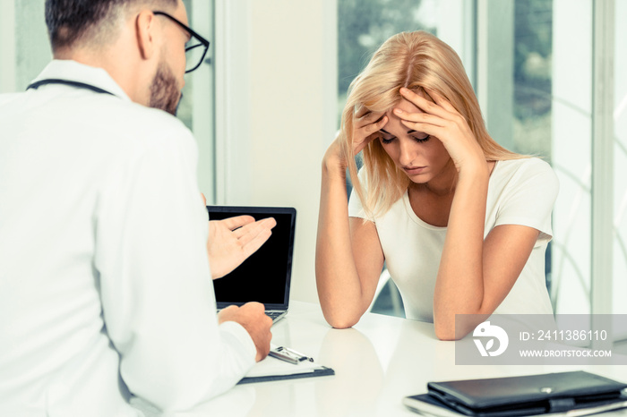 Male doctor is talking to serious female patient in hospital office. Healthcare and medical service.