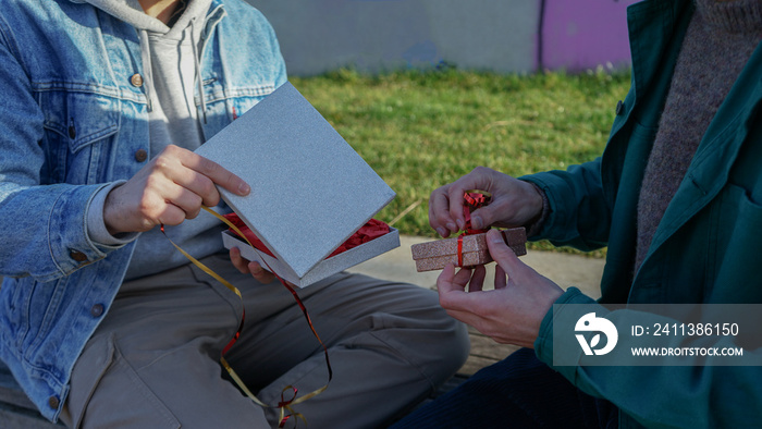 Close-up of gay couple opening gift boxes outdoors