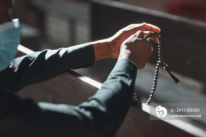 Close-up of priest in mask holding rosary beads while sitting in front of the altar