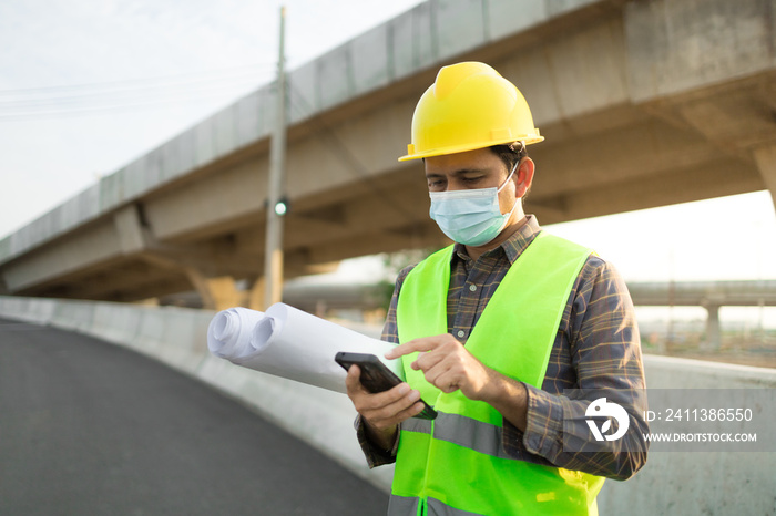 asian man construction worker wear protective face masks and user smart phone against construction site background