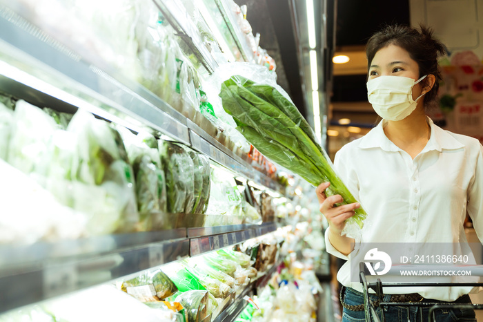 new normal after covid epidemic young smart asian female shopping new lifestyle in supermarket with face shild or mask protection hand choose fresh vegetable of fruit new normal lifestyle