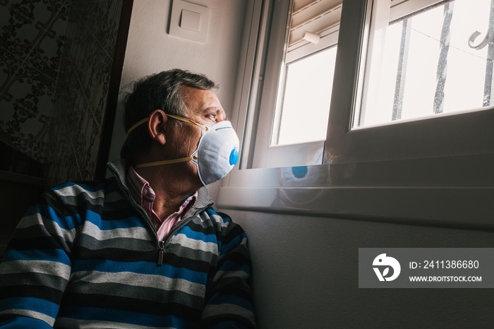 Selective focus of man with a mask confined in quarantine to prevent coronavirus spread to the window.