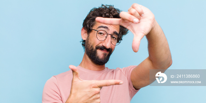 young bearded man feeling happy, friendly and positive, smiling and making a portrait or photo frame with hands