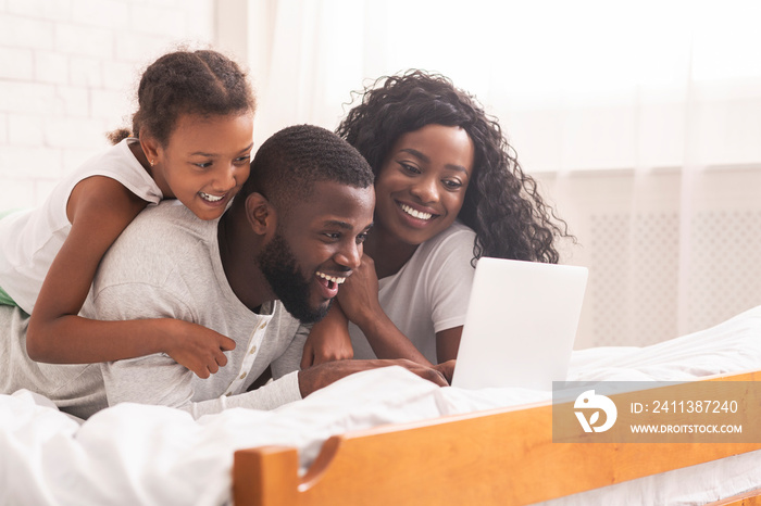 African family lying on bed browsing internet on laptop together