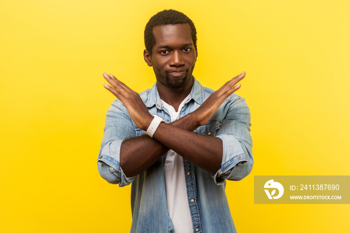 Never again. Portrait of absolutely convinced man in denim casual shirt standing crossing hands, showing x sign meaning stop, there is no way, finish. indoor studio shot isolated on yellow background