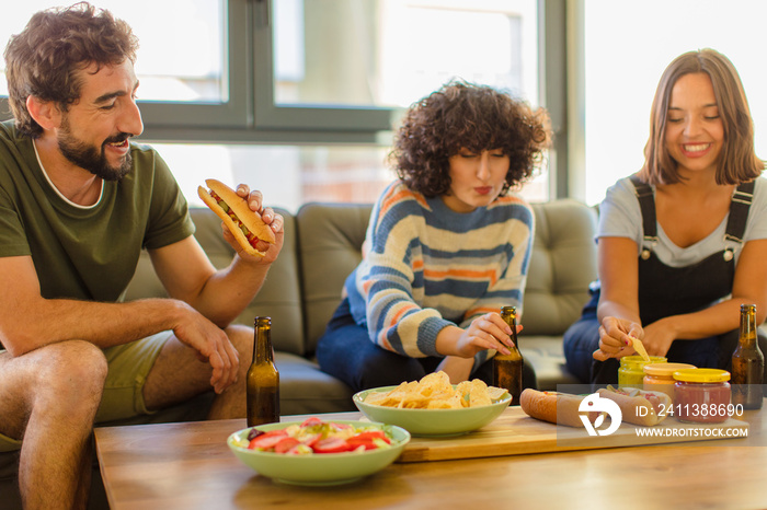 group of young friends enjoying, drinking and eating at new home