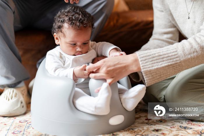 Mather holding baby daughter sitting on infant seat at home