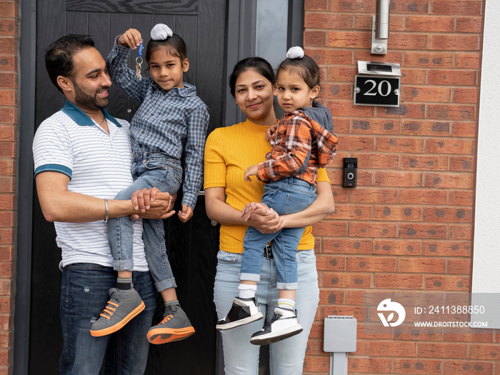 Portrait of family (2-3,6-7) standing on front porch and holding keys to house