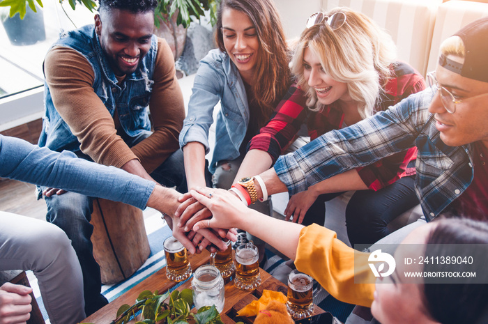 Group of mixed friends with stack of hands showing unity and teamwork.