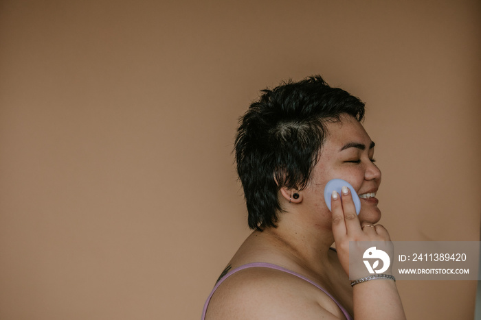 portrait of a plus size filipino woman applying sponge to skin