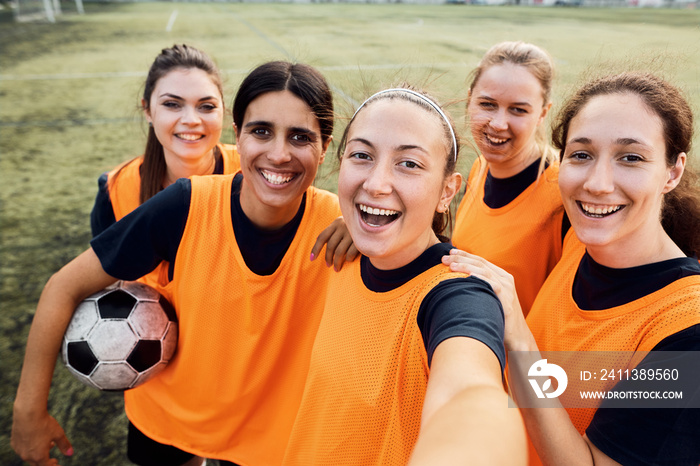 Cheerful women’s soccer team taking selfie at stadium.