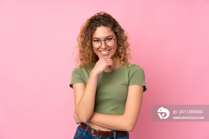 Young blonde woman with curly hair isolated on pink background with glasses and smiling