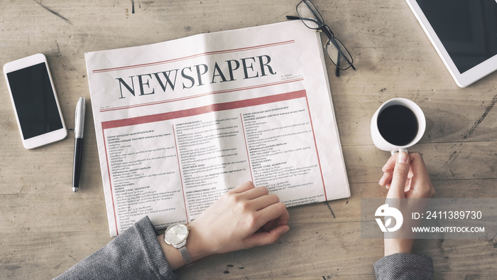 Woman reading newspaper and drinking coffee on table