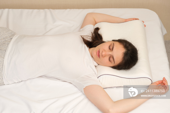 A woman sleeps on an orthopedic pillow made of memory foam, lying on a bed. The correct pillow for a comfortable healthy sleep.