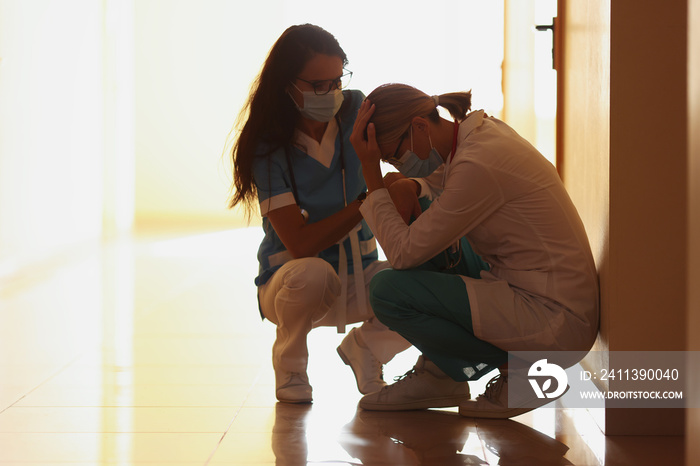 Tired doctors in protective medical mask sit on corridor